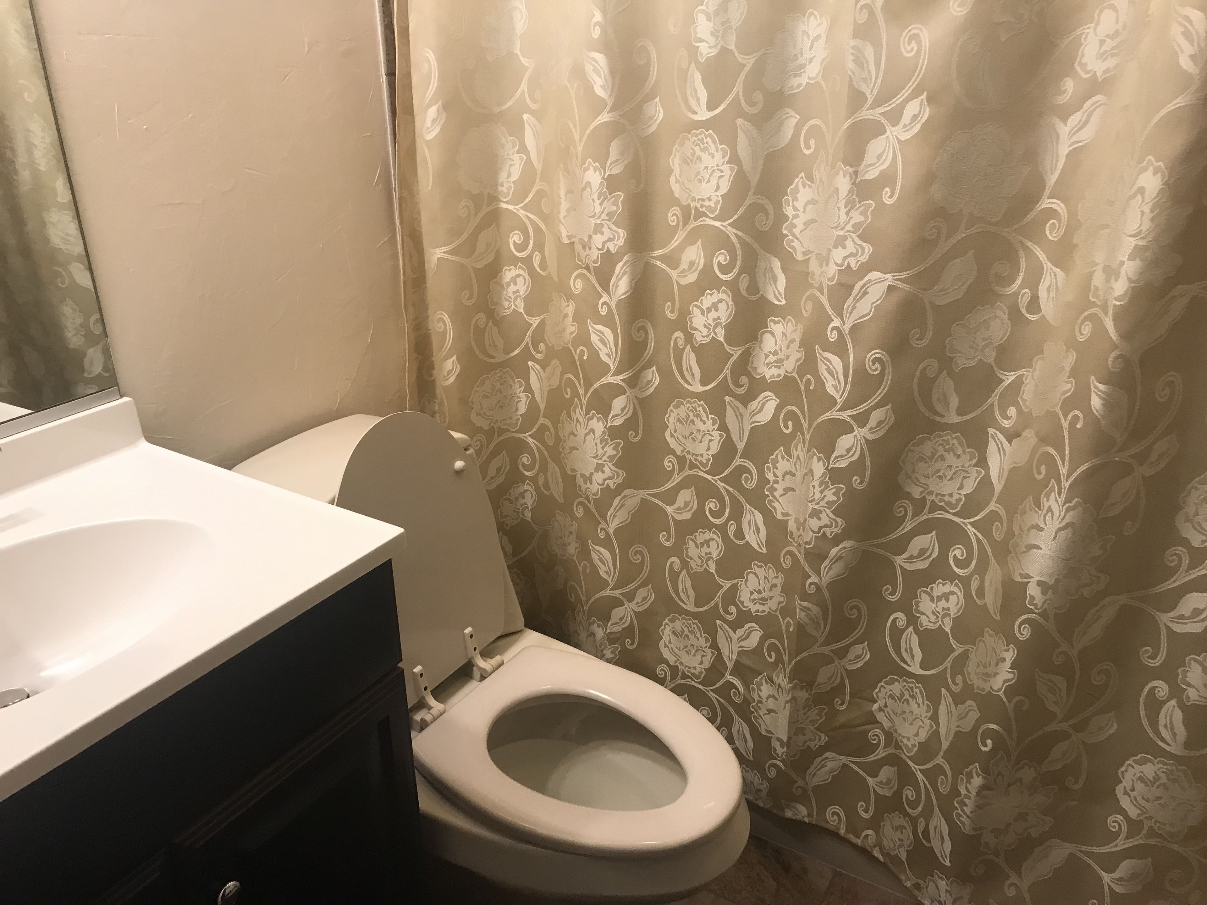 Un baño con inodoro, lavabo y cortina de ducha con estampado floral.