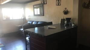 A kitchen with a dark countertop, a black leather sofa, a hanging mirror, and pendant lights. - North Wind Condo (Angel Fire)