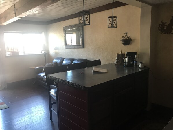 A kitchen with a dark countertop, a black leather sofa, a hanging mirror, and pendant lights.