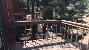 A wooden deck with metal chairs and a table, overlooking a parking area and trees. - North Wind Condo (Angel Fire)