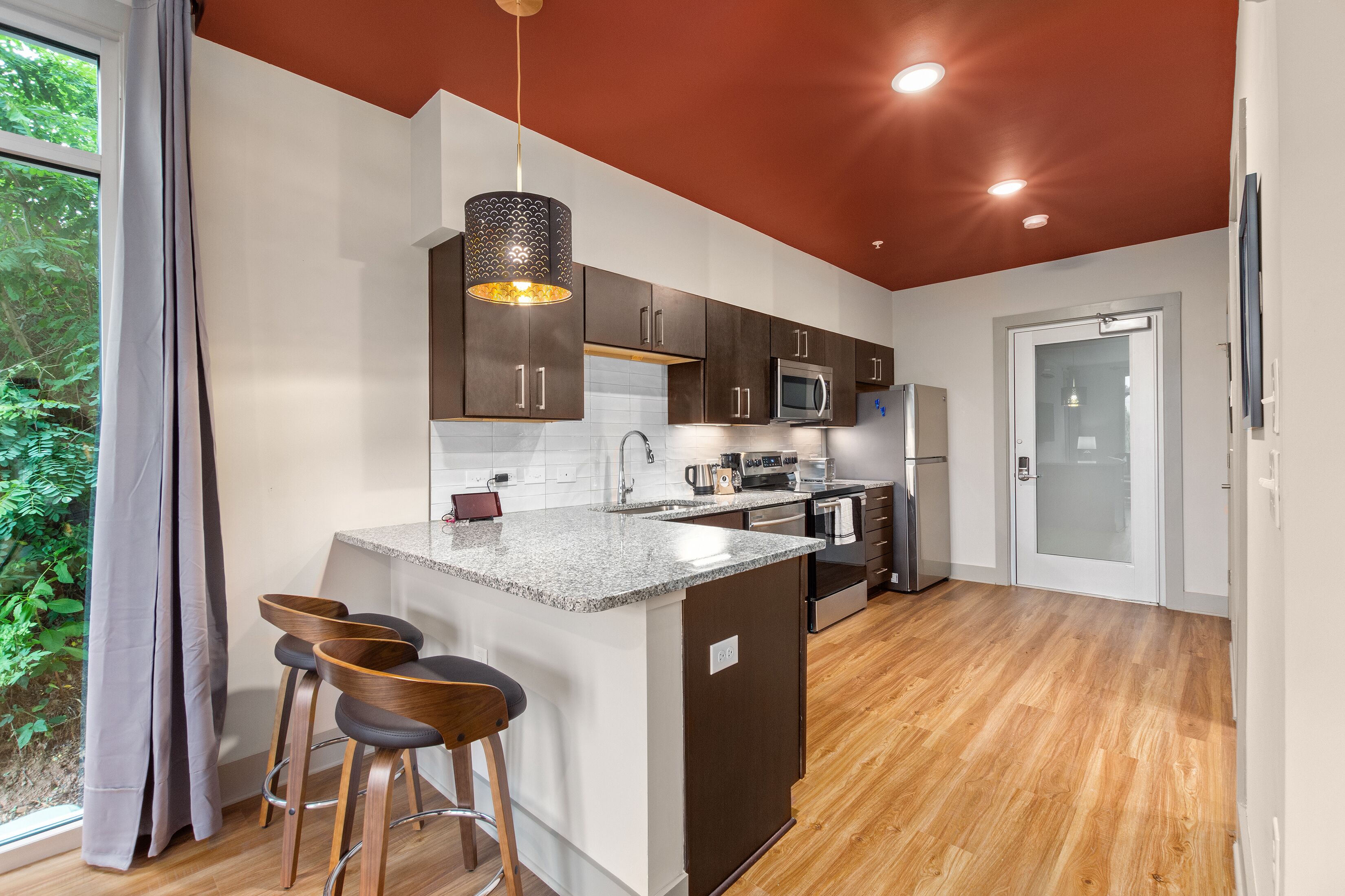 A modern kitchen with a central island, bar stools, and a view of greenery outside.