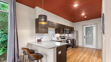A modern kitchen with a central island, bar stools, and a view of greenery outside.