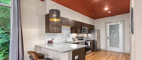 A modern kitchen with a central island, bar stools, and a view of greenery outside.