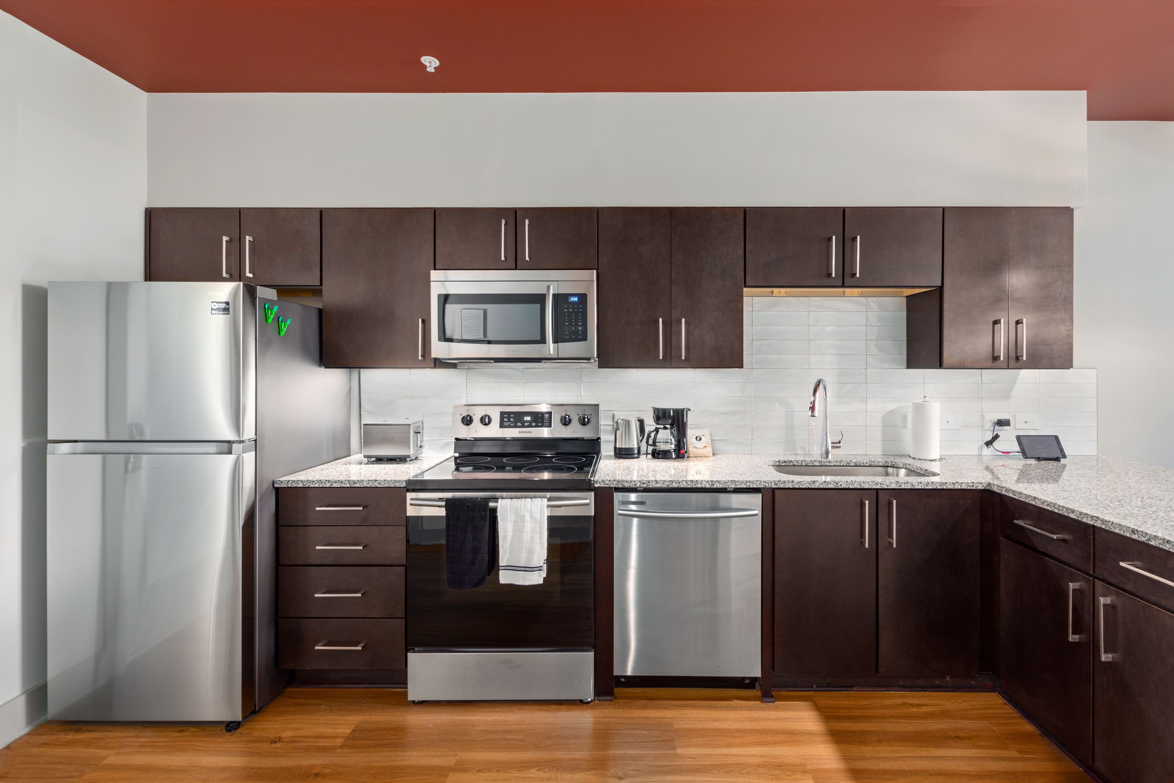 A modern kitchen with stainless steel appliances, dark wooden cabinets, and a granite countertop.