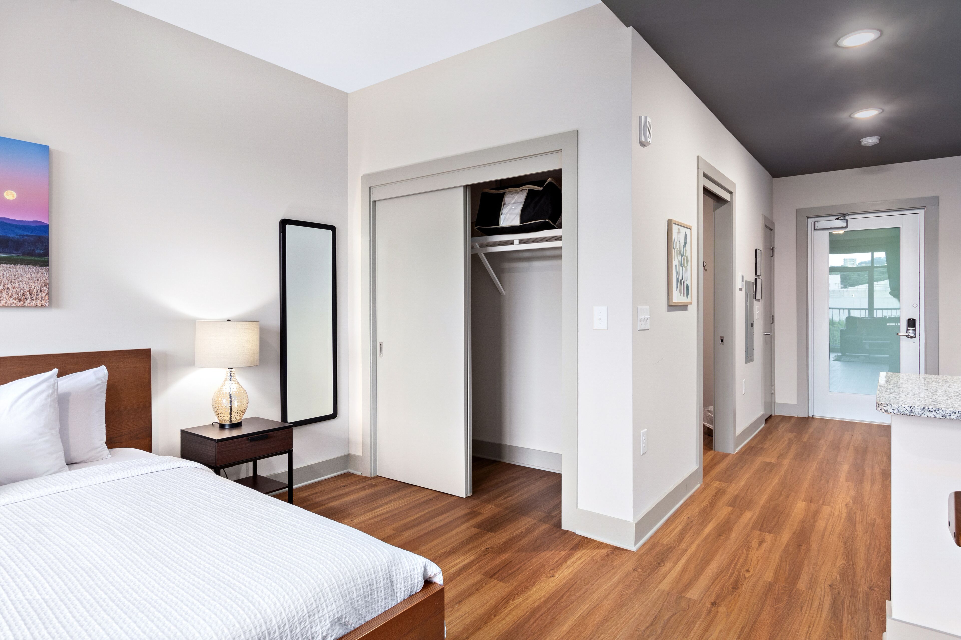Ein Hotelzimmer mit Bett, Nachttischlampe, Holzboden, Schrank und Blick ins Freie.