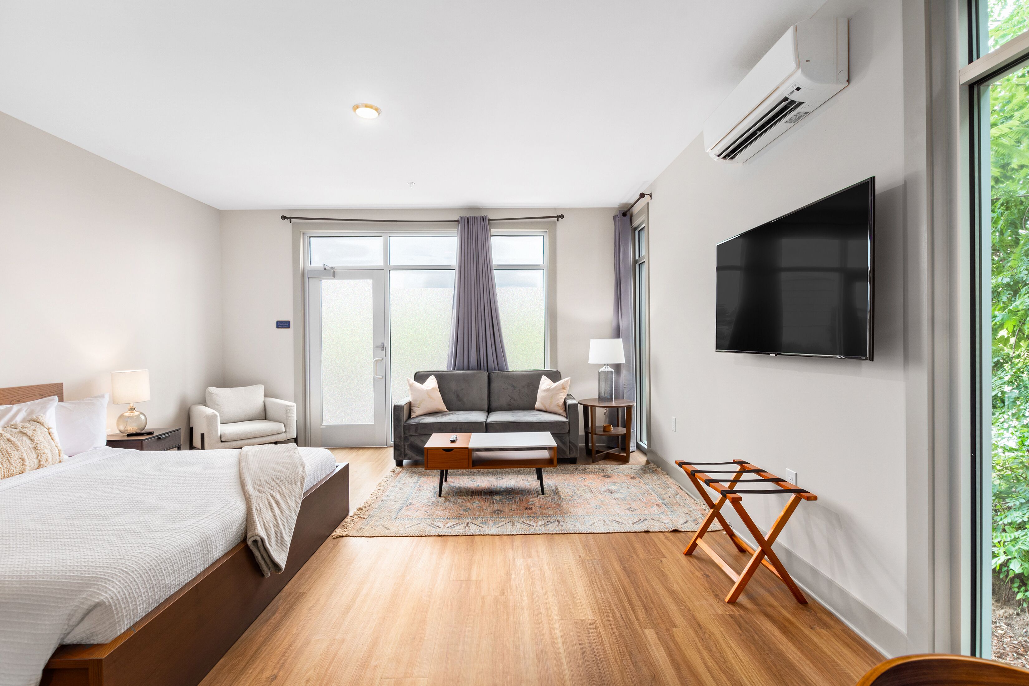 A modern hotel room with a large bed, a sofa, a TV, and a window with curtains.