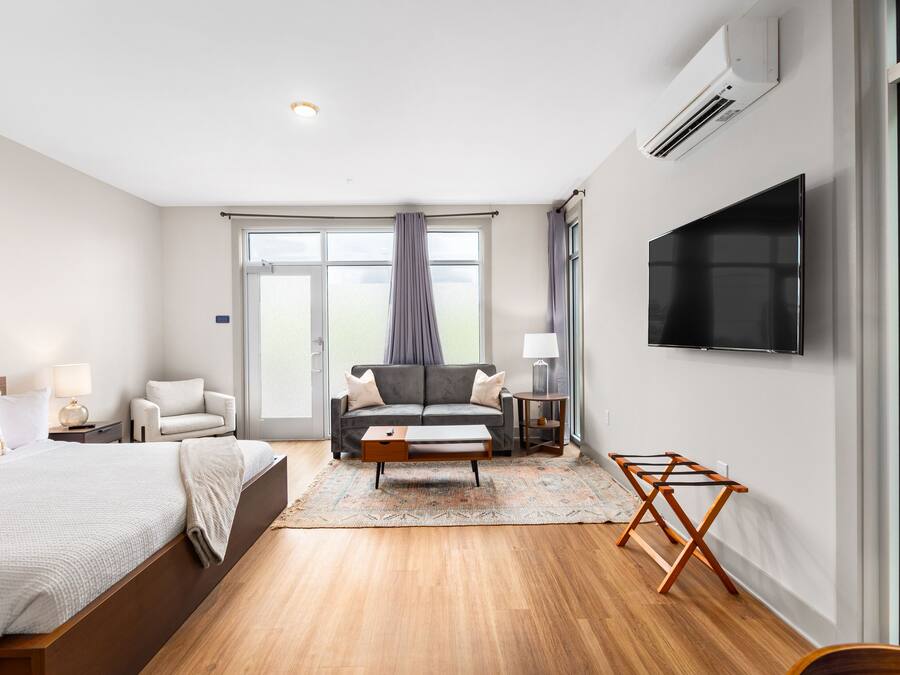A modern hotel room with a large bed, a sofa, a TV, and a window with curtains.