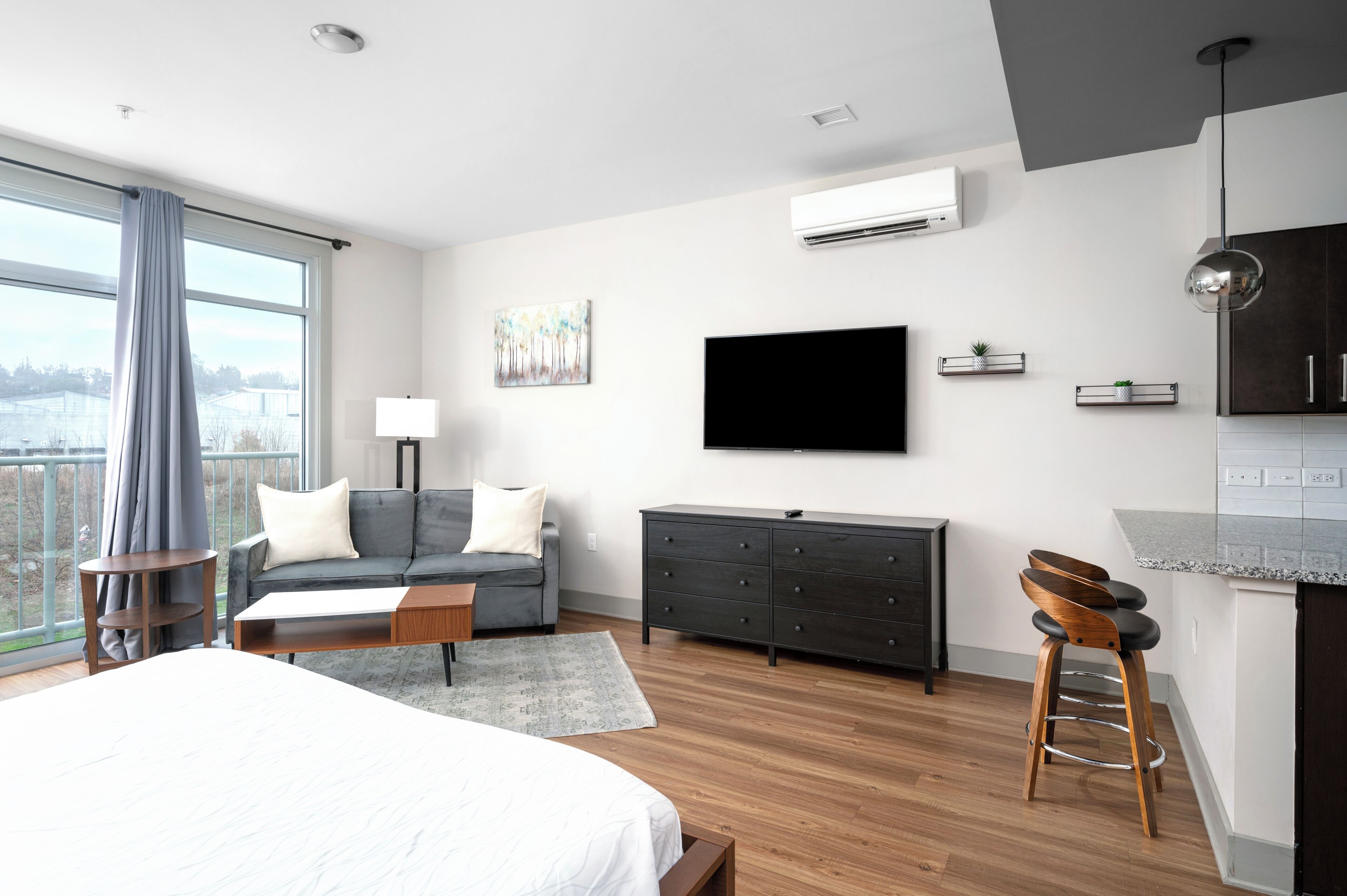 Habitación de hotel moderna con una cama grande, un sofá, un televisor, un aparador y vistas a la ciudad.