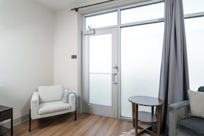 A modern room with a sliding glass door, a small round table, a sofa, and a chair. - River Row Flats (Asheville)
