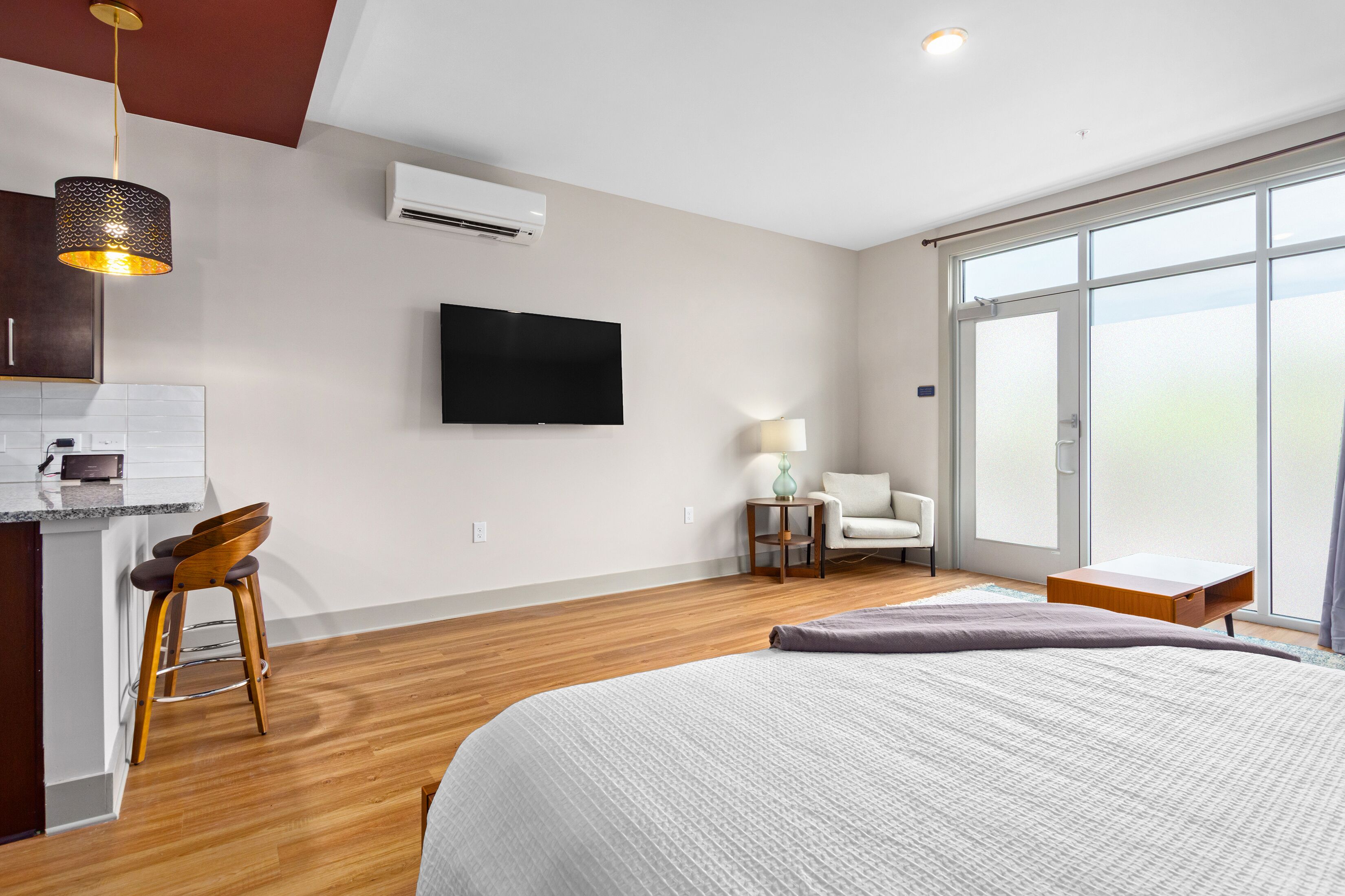 A modern hotel room with a large bed, a TV mounted on the wall, a wooden floor, and a large window offering a view.
