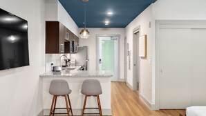 A modern kitchen with a central island, two bar stools, and wooden flooring. - River Row Flats (Asheville)