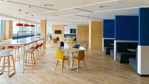 A modern dining area with high tables and chairs, a kitchen in the background, and a blue accent wall. - Holiday Inn Express Shanghai Jiading New City by IHG (Shanghai)