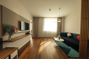 A modern living room with a flat-screen TV, wooden flooring, a sofa, a coffee table, and a dining area with a table and chairs.
