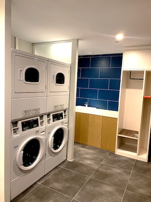 A laundry room with stacked washing machines, a blue tiled wall, and a wooden cabinet. - Holiday Inn Express Shanghai Jiading New City by IHG (Shanghai)