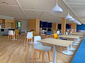 A modern dining area with multiple tables and chairs, a kitchen area, and a blue wall. - Holiday Inn Express Shanghai Jiading New City by IHG (Shanghai)