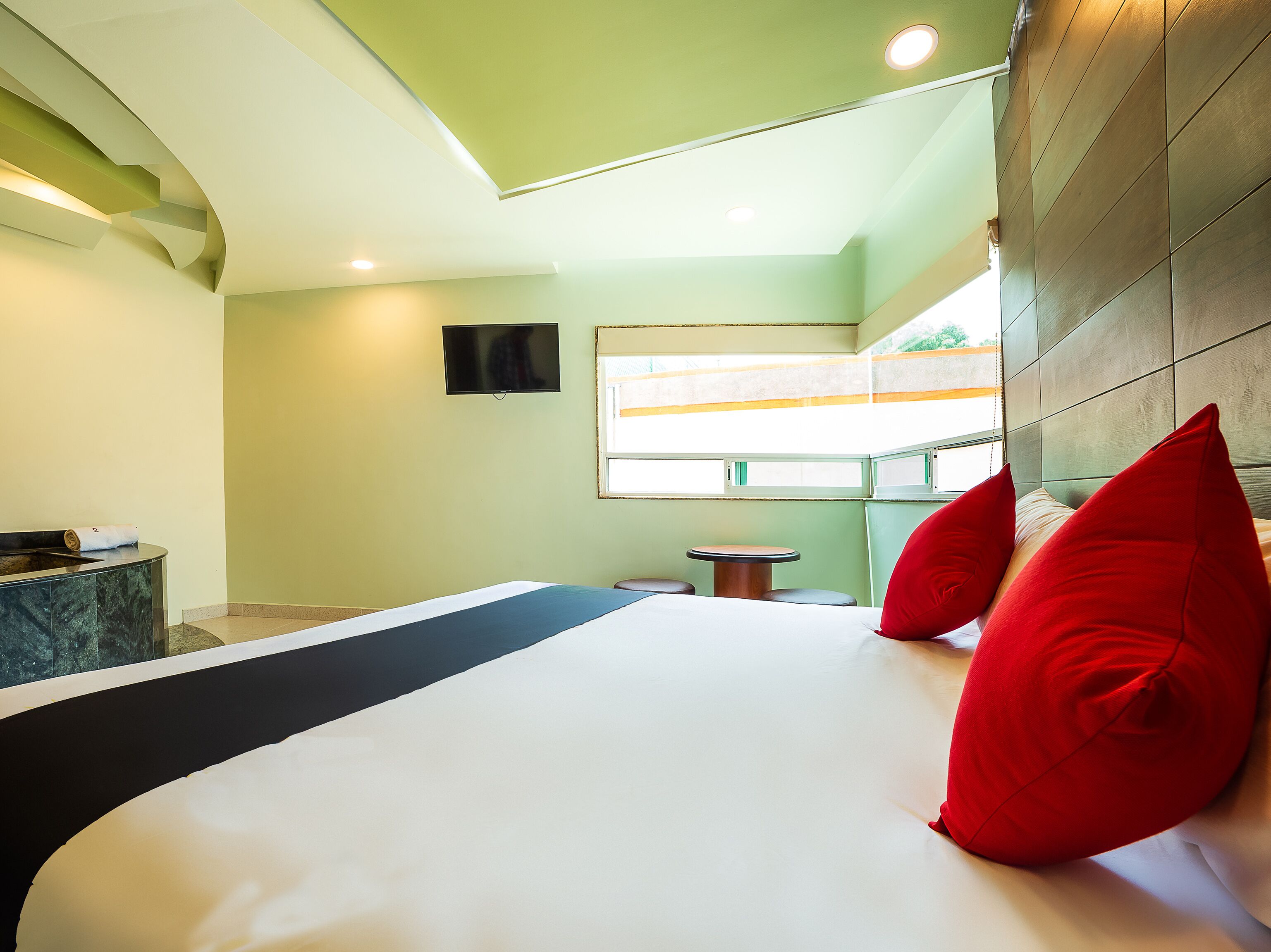 A hotel room with a bed, a TV, a window, and a small table.