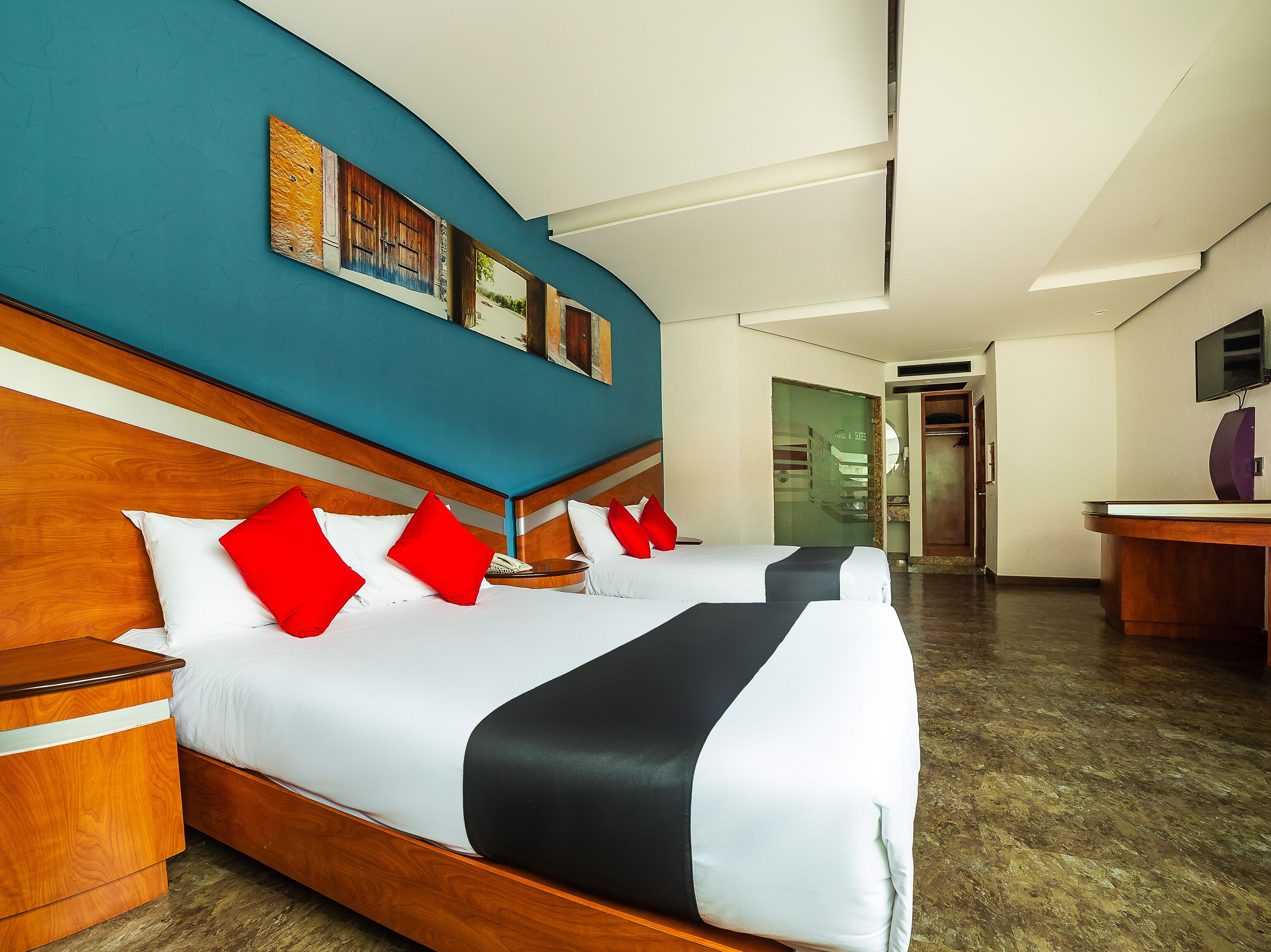 A hotel room with a large bed, wooden headboard, and a blue accent wall.