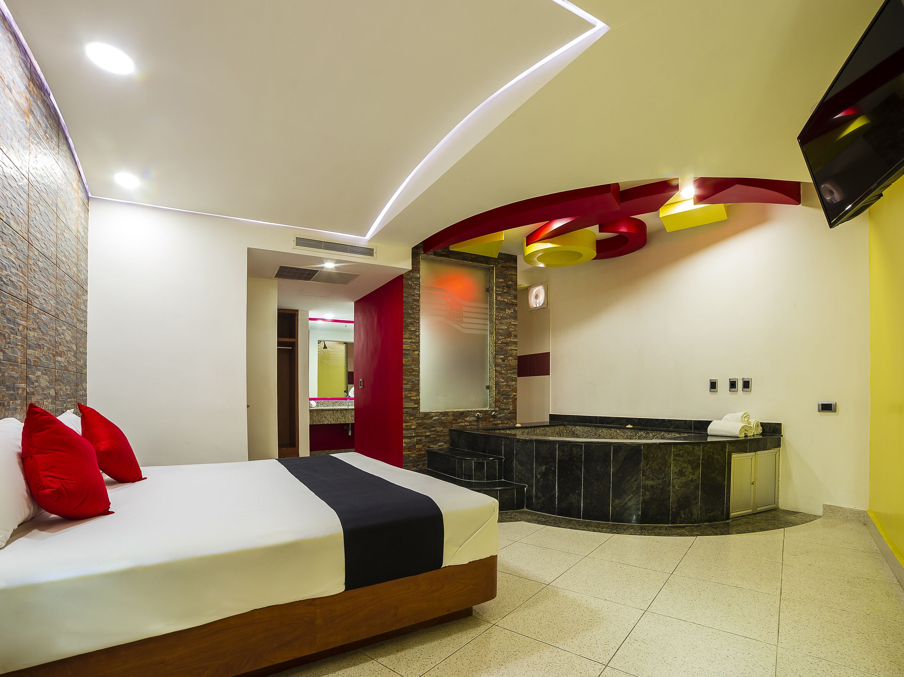 Habitación de hotel moderna con una cama grande, un baño con bañera y un televisor montado en la pared.