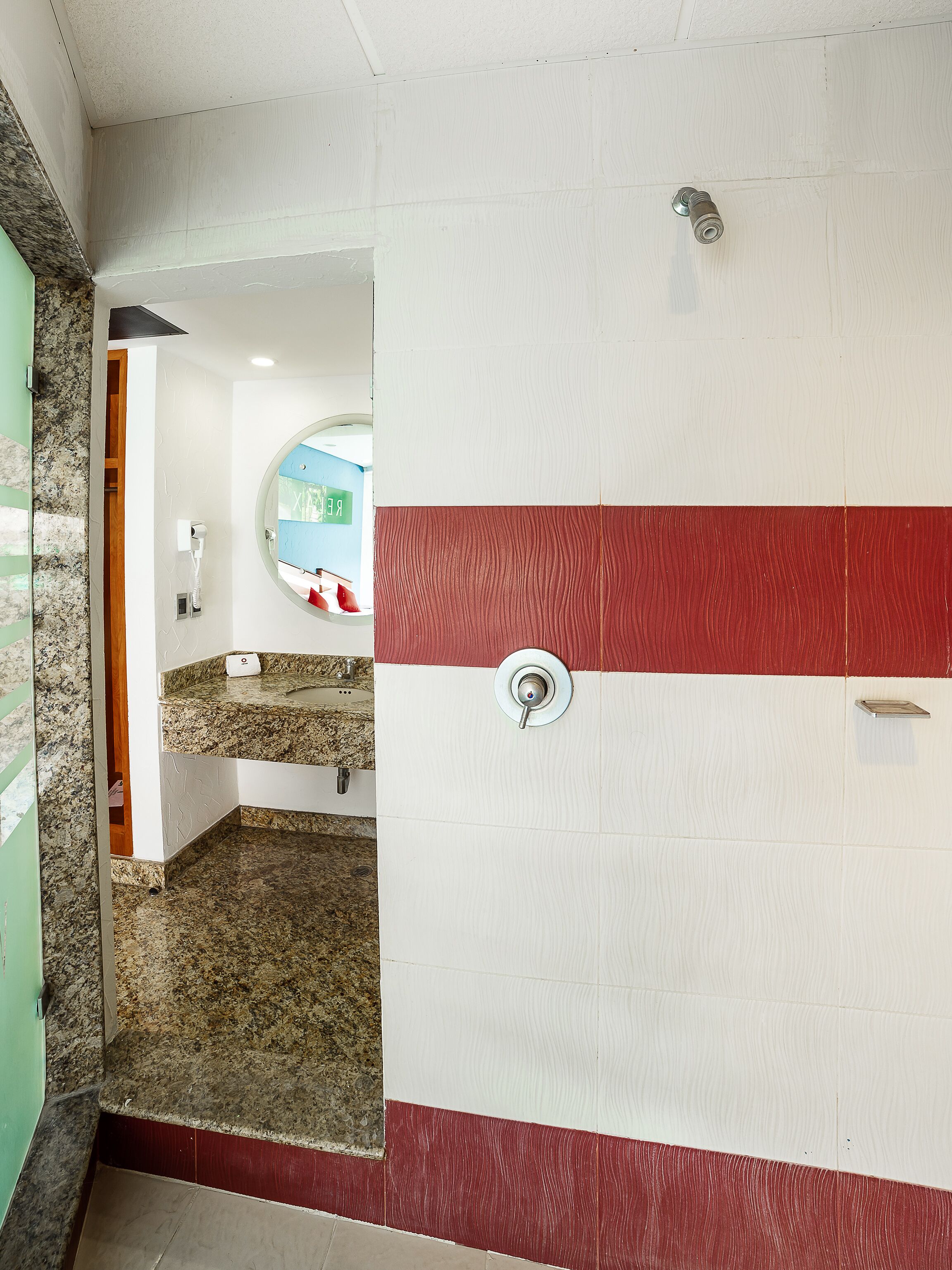 A bathroom with a white and red tiled wall, a granite countertop, and a shower area.