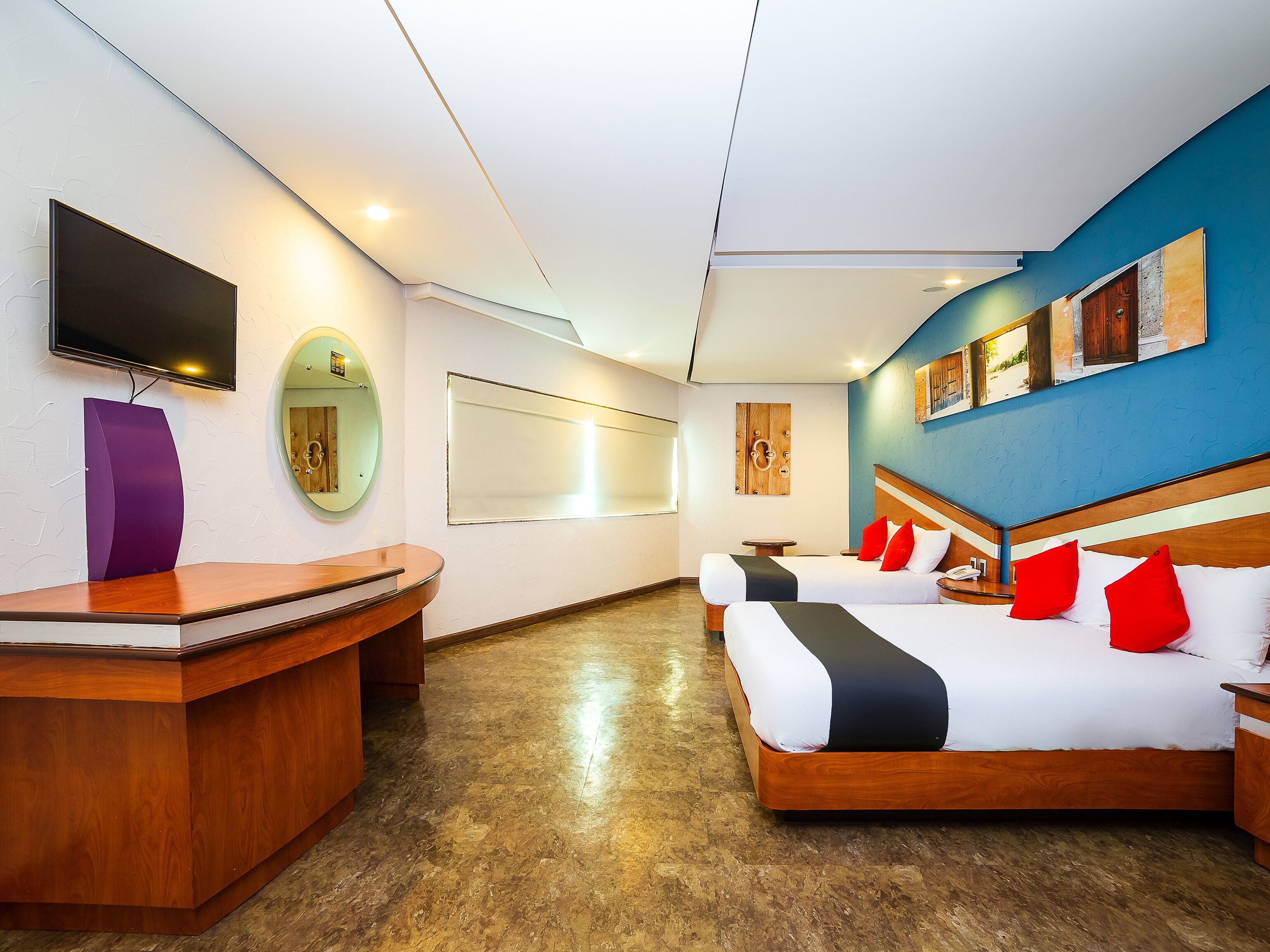 A hotel room with two beds, a desk, a TV, and artwork on the walls.