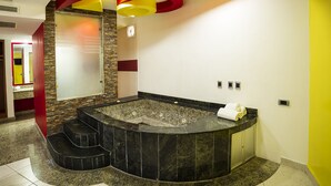A modern bathroom with a curved marble tub, a stone accent wall, and a red and yellow abstract ceiling design. - Hotel Verona (Tlalnepantla de Baz)