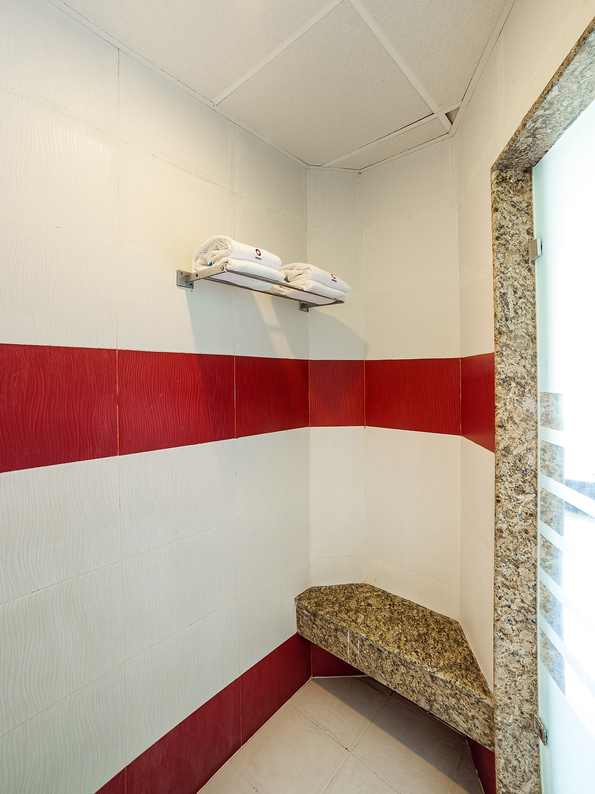 Een hoek van een kamer met witte en rode wanden, een metalen handdoekrek met handdoeken, en een granieten aanrechtblad.