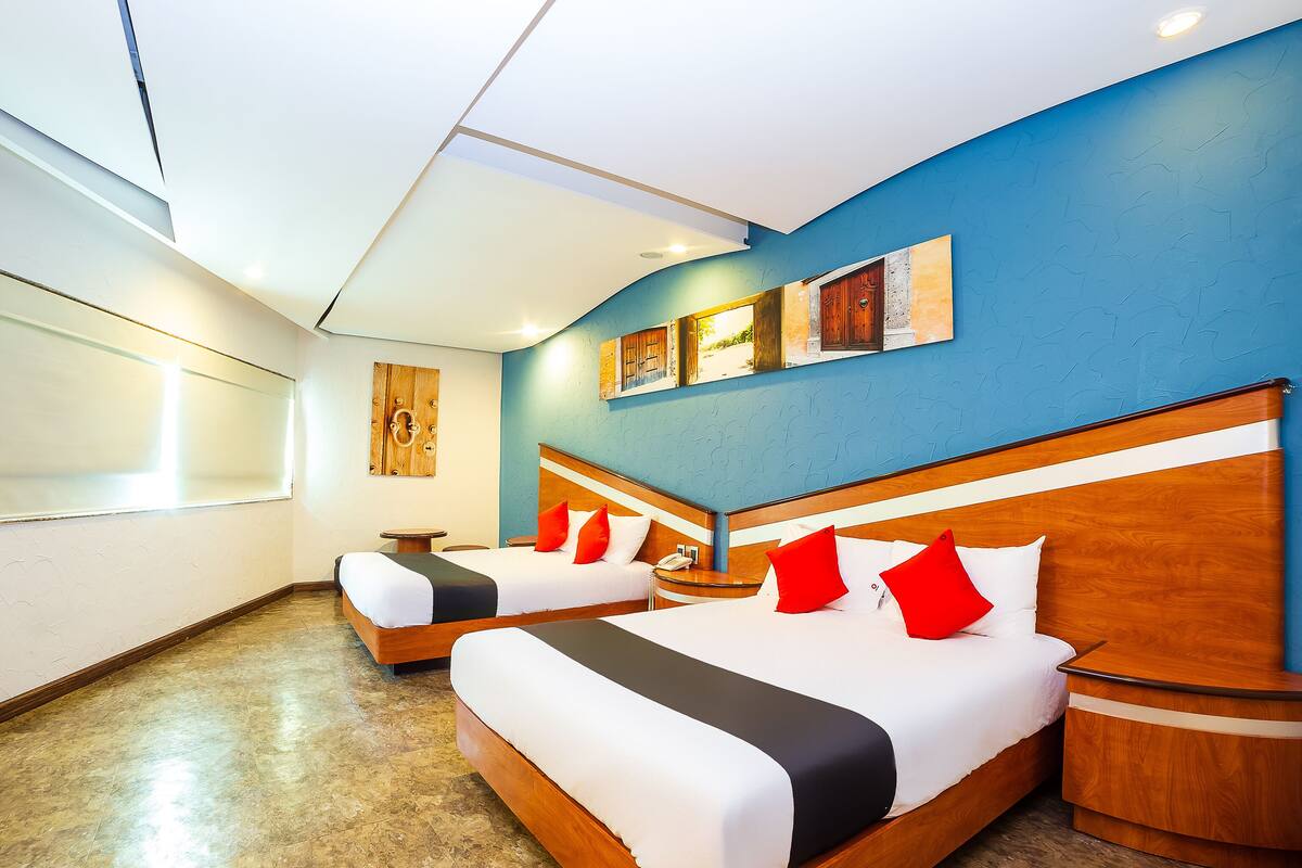 A hotel room with two beds, a wooden headboard, a small round table, and a wall-mounted artwork.