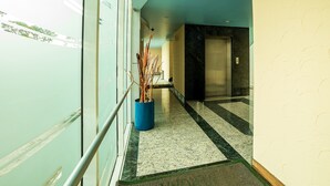 A hallway with a blue ceiling, a potted plant, a marble floor, and a door with an elevator. - Hotel Verona (Tlalnepantla de Baz)