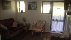 A living room with a sofa, two chairs, a small table, and a window with curtains. - Monty's self-contained unit (Kawhia)