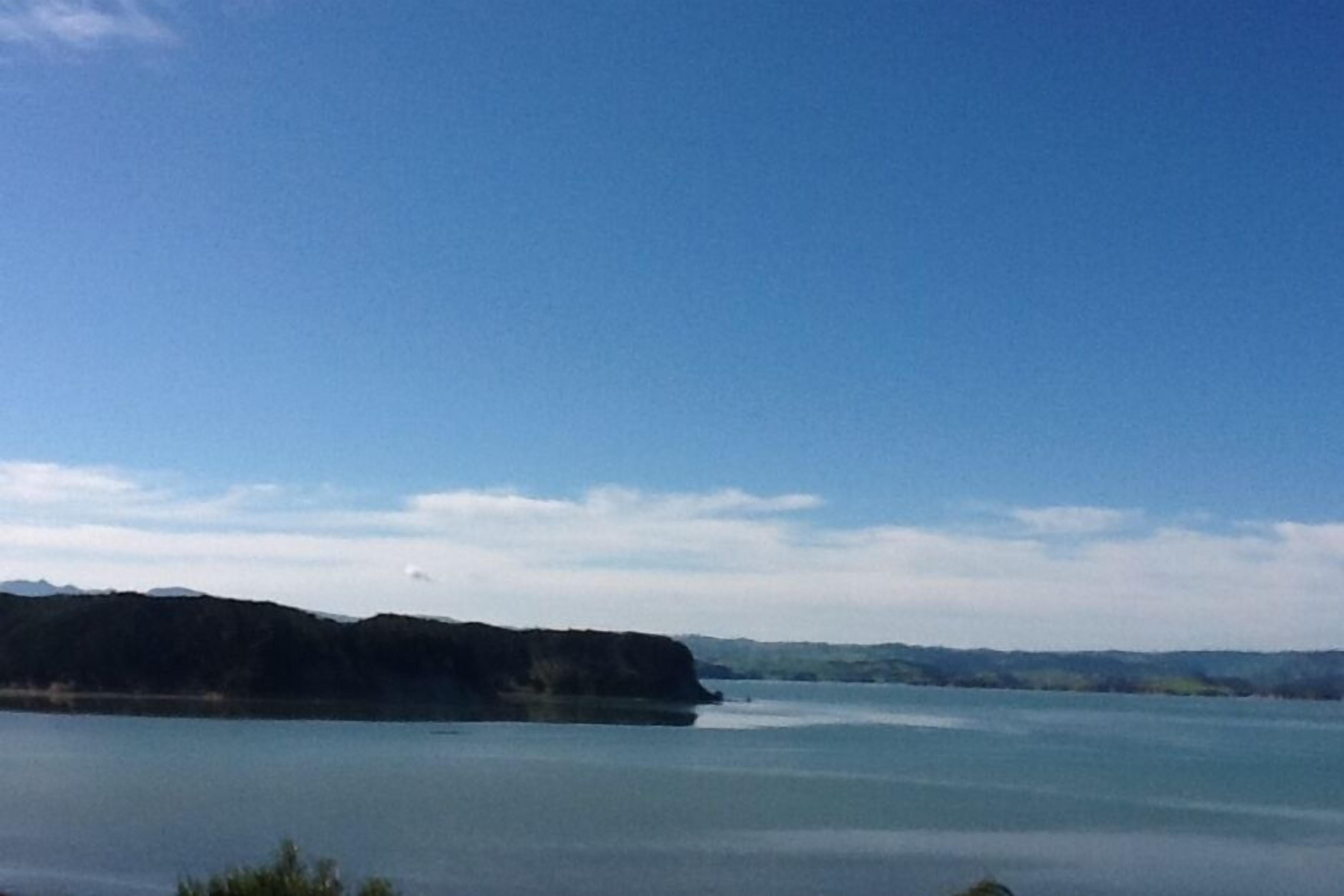 Eine Küstenlandschaft mit ruhigem Gewässer, einer fernen Küstenlinie und blauem Himmel.