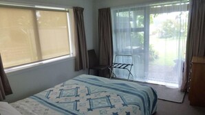 A hotel room with a bed, a chair, a small table, and a view of the outdoors. - Monty's self-contained unit (Kawhia)