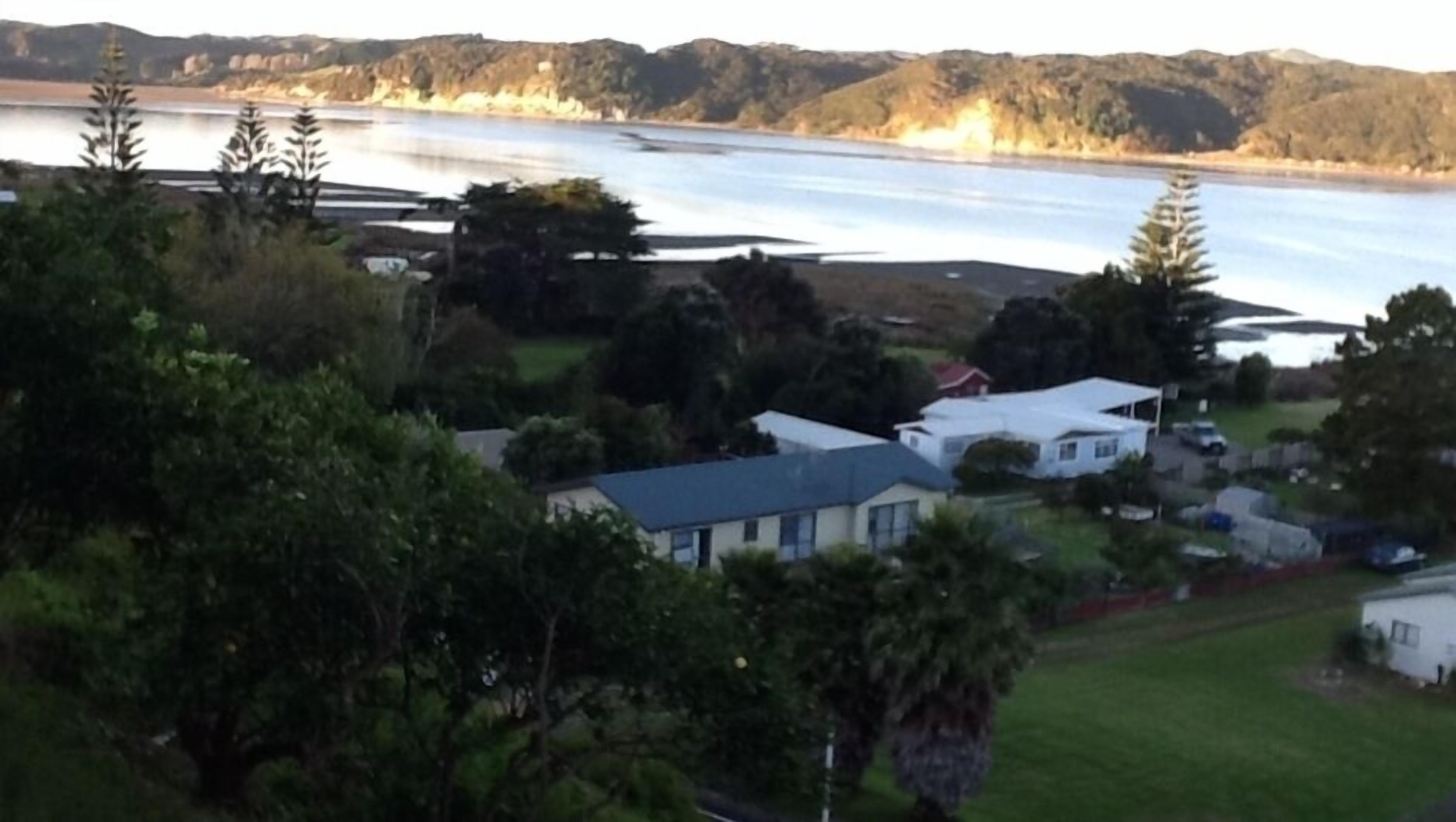 Ett bostadsområde med hus, en sjö eller ett annat vattendrag och kullar i bakgrunden.