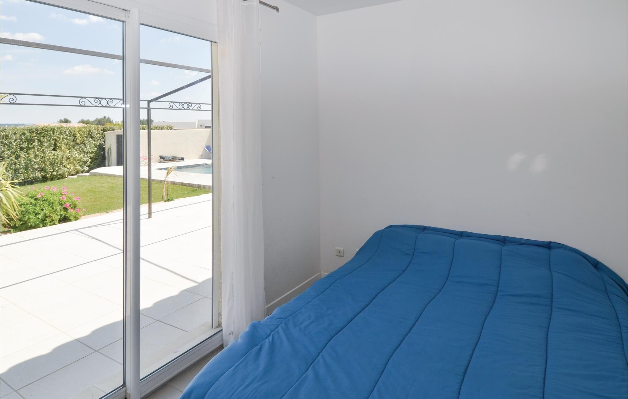 Een slaapkamer met een bed, een schuifdeur naar een balkon met zwembad en tuin.