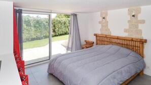 Quarto com cama grande, cabeceira de madeira, mesinha de cabeceira e porta de vidro deslizante para uma varanda.