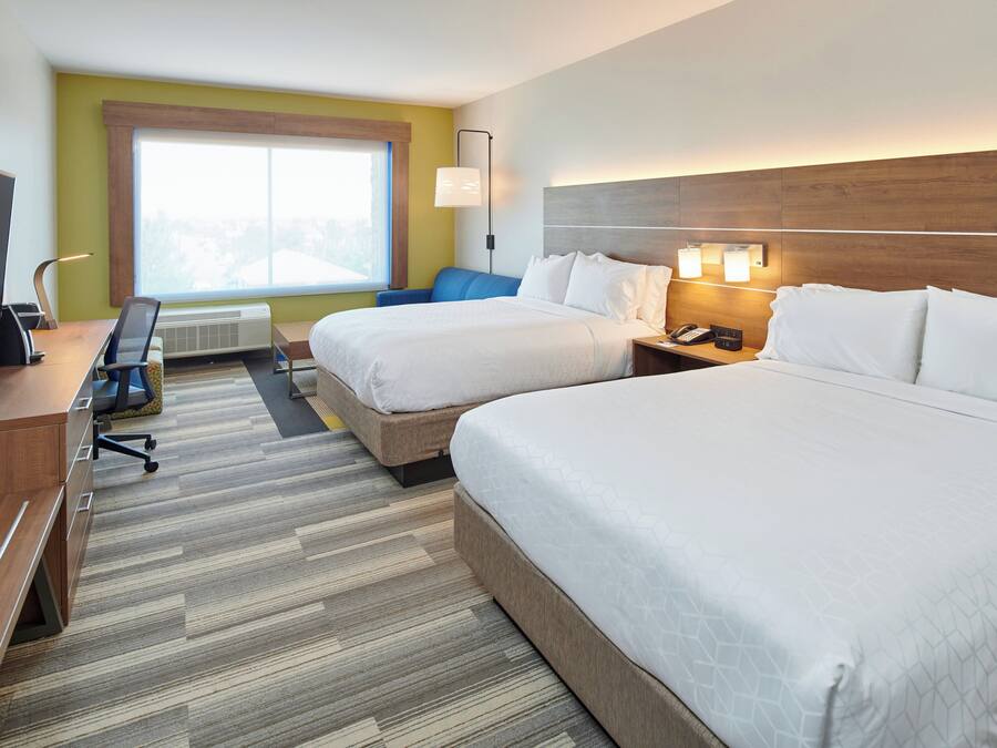 A hotel room with two beds, a desk, a chair, a TV, and a window with a view.
