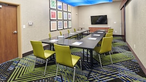 Un salón de conferencias con una larga mesa, sillas amarillas, obras de arte enmarcadas en la pared y un televisor de pantalla plana.