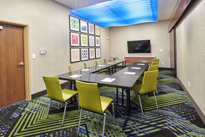 Un salón de conferencias con una larga mesa, sillas amarillas, obras de arte enmarcadas en la pared y un televisor de pantalla plana.