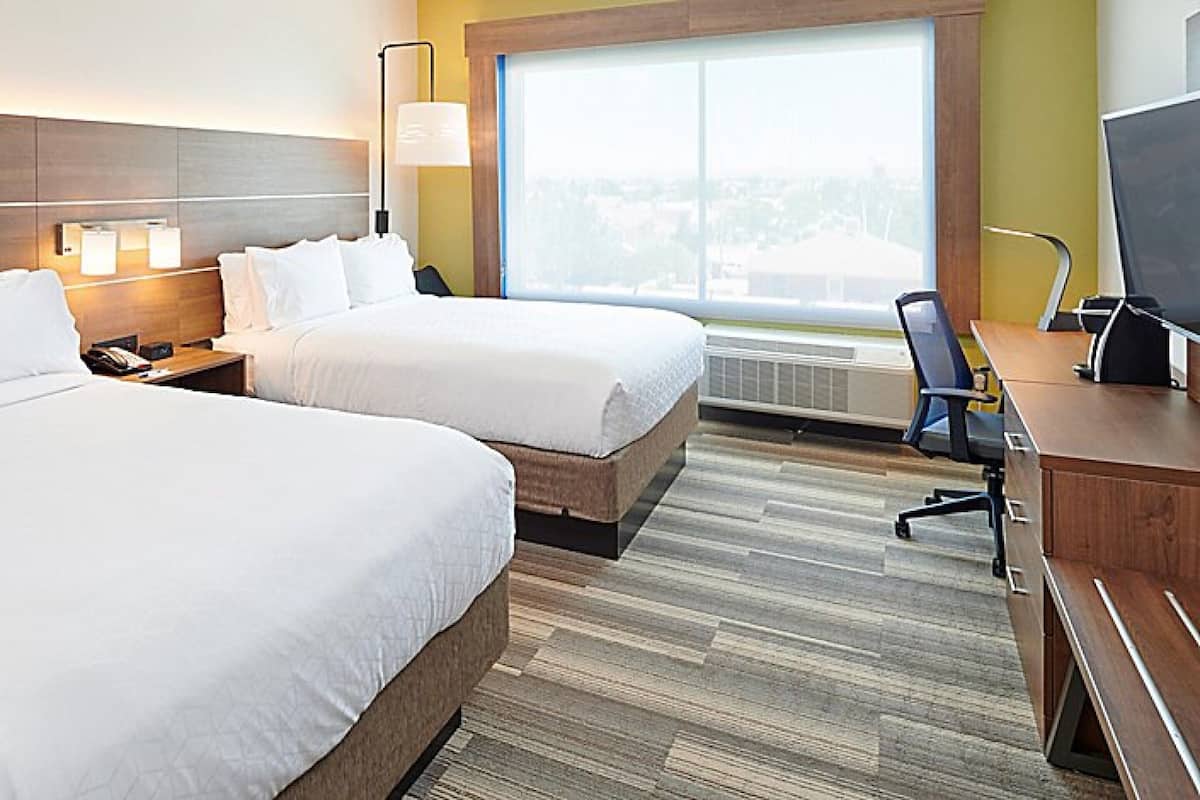 Een hotelkamer met twee bedden, een bureau, een stoel, een lamp en een groot raam.