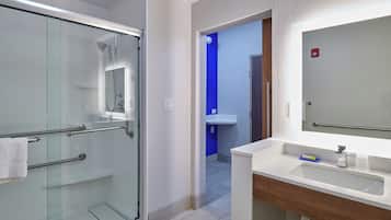 A modern bathroom with a glass shower enclosure, a white sink with a wooden vanity, and a blue accent wall.