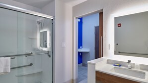 Uma casa de banho moderna com chuveiro em cabine de vidro, pia branca com toucador de madeira e parede de destaque azul.