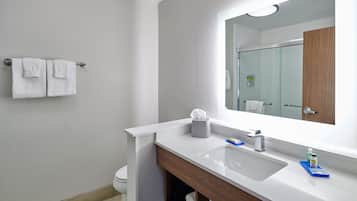 A modern bathroom with a white sink, wooden vanity, and a large mirror.