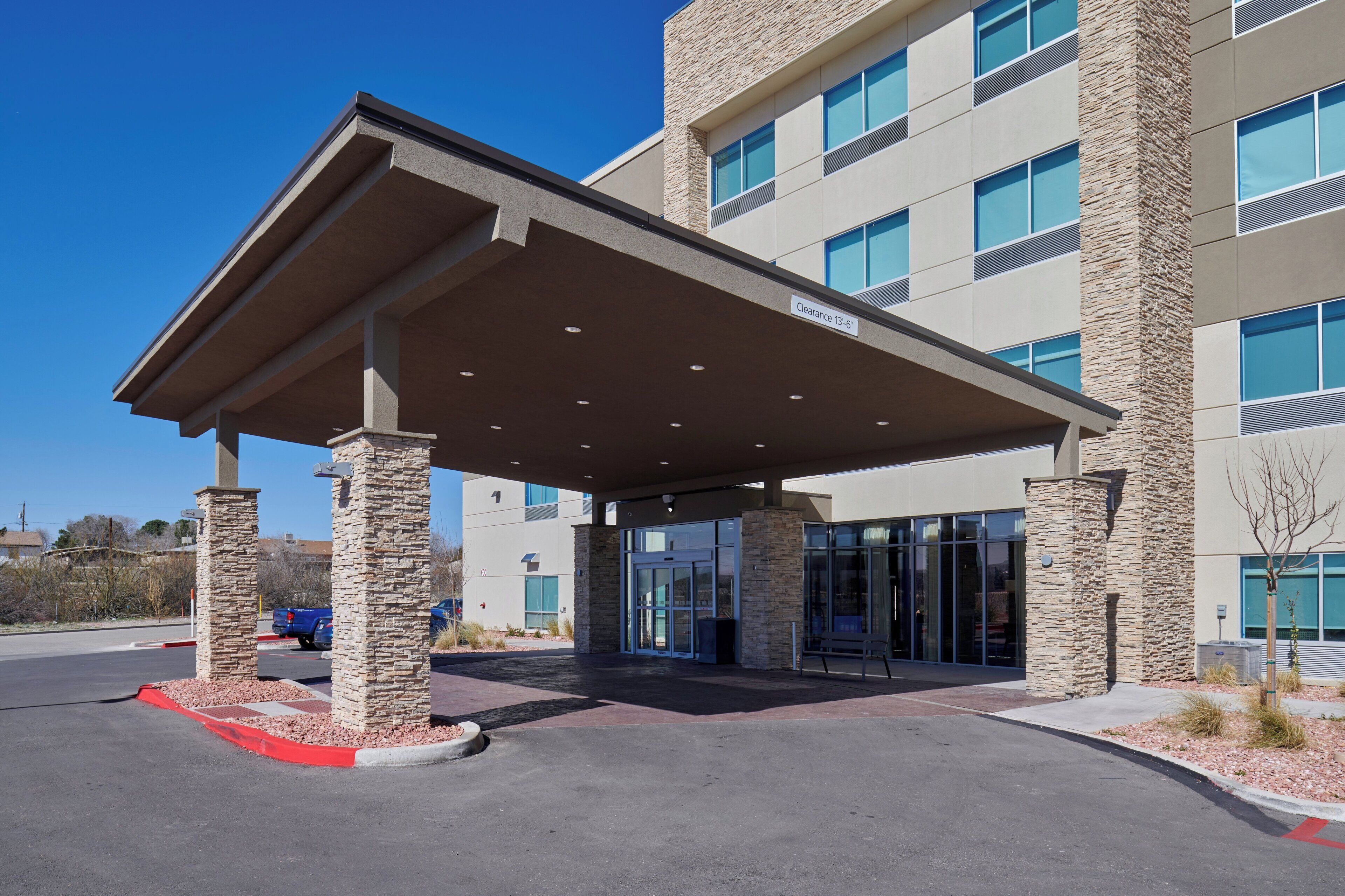 A building with a covered entrance, stone pillars, and a clear blue sky.