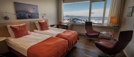 A hotel room with two beds, a desk, a chair, and a large window with a view of a snowy landscape.