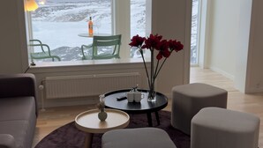 A modern living room with a large window, a round table, two ottomans, a sofa, and a decorative lamp. - Hotel Arctic (Ilulissat)