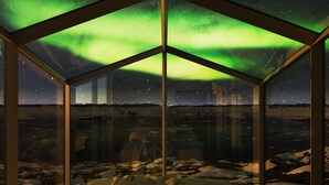 A glass enclosure with a view of the northern lights and a snowy landscape. - Hotel Arctic (Ilulissat)