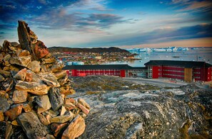 A coastal town with a prominent red building, rocky terrain, and icebergs in the background.