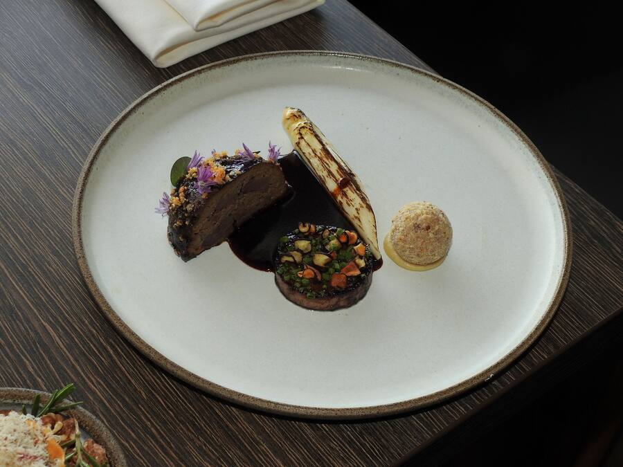 A plate with a piece of meat, a vegetable, and a small mound of rice on a dark wooden table.