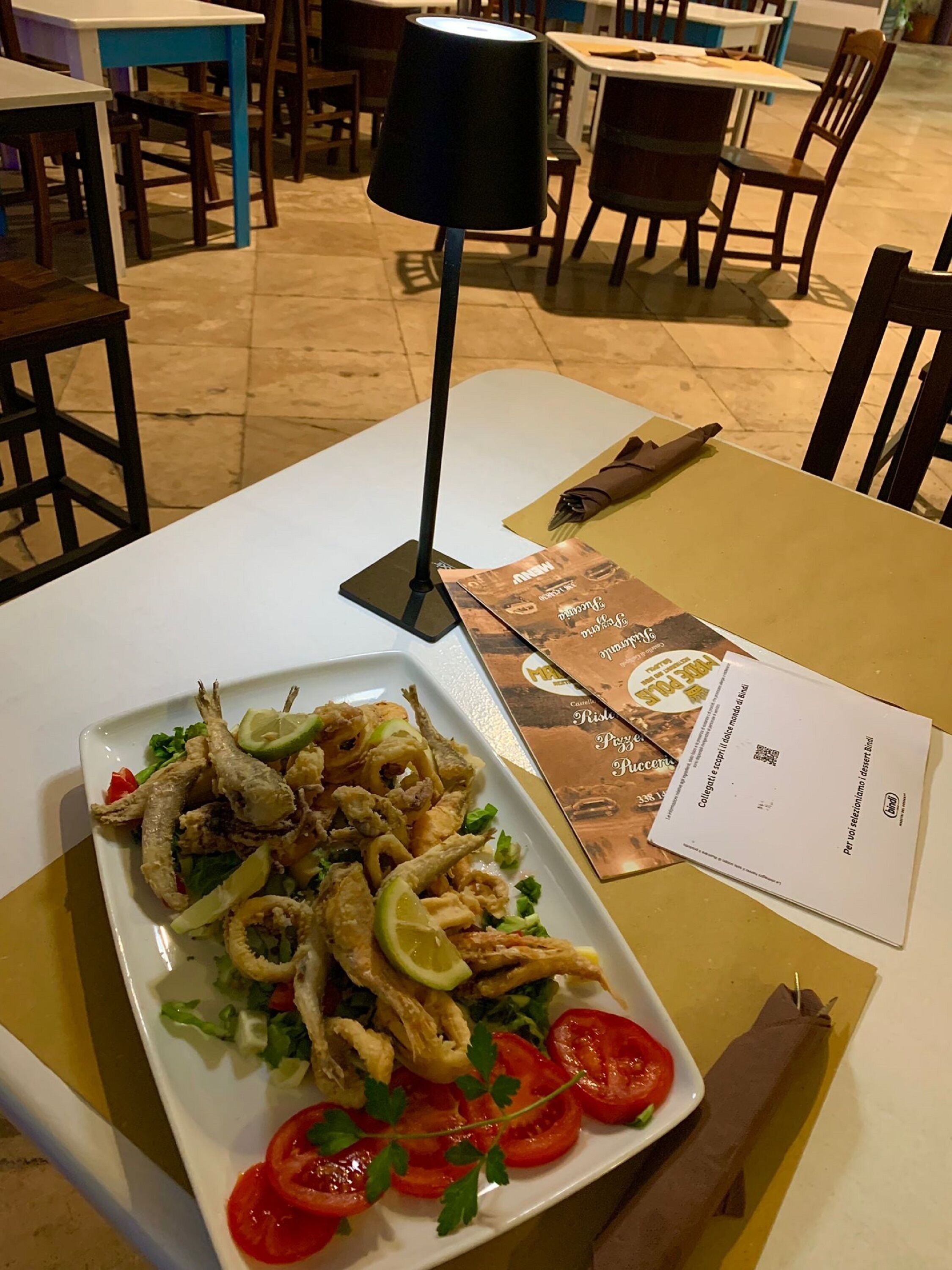 Una mesa de comedor con un plato de comida, un menú y una lámpara negra.