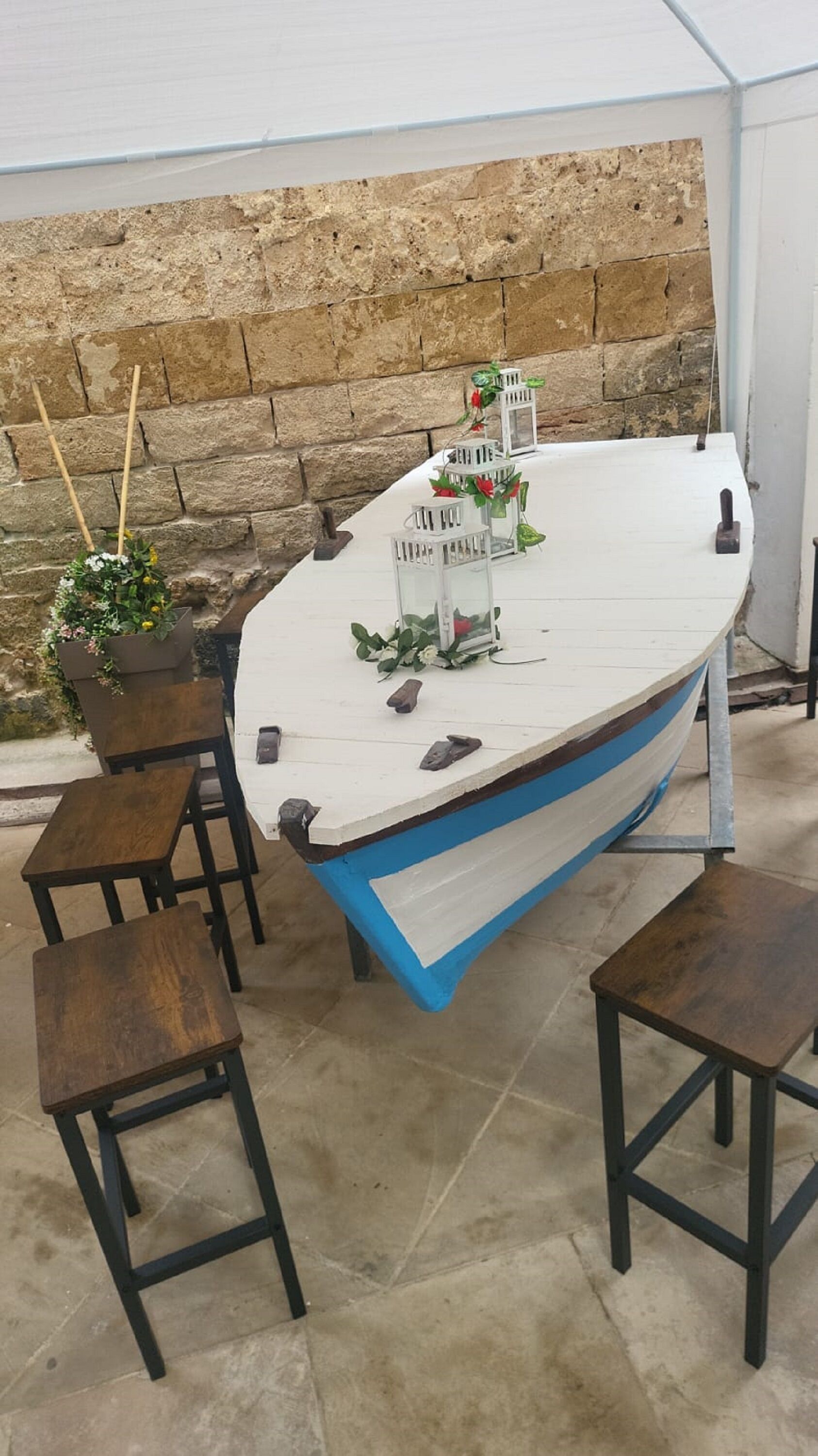 Een boot met een witte bovenkant en een blauwe onderkant, staand op een betonnen vloer met een stenen muur op de achtergrond.