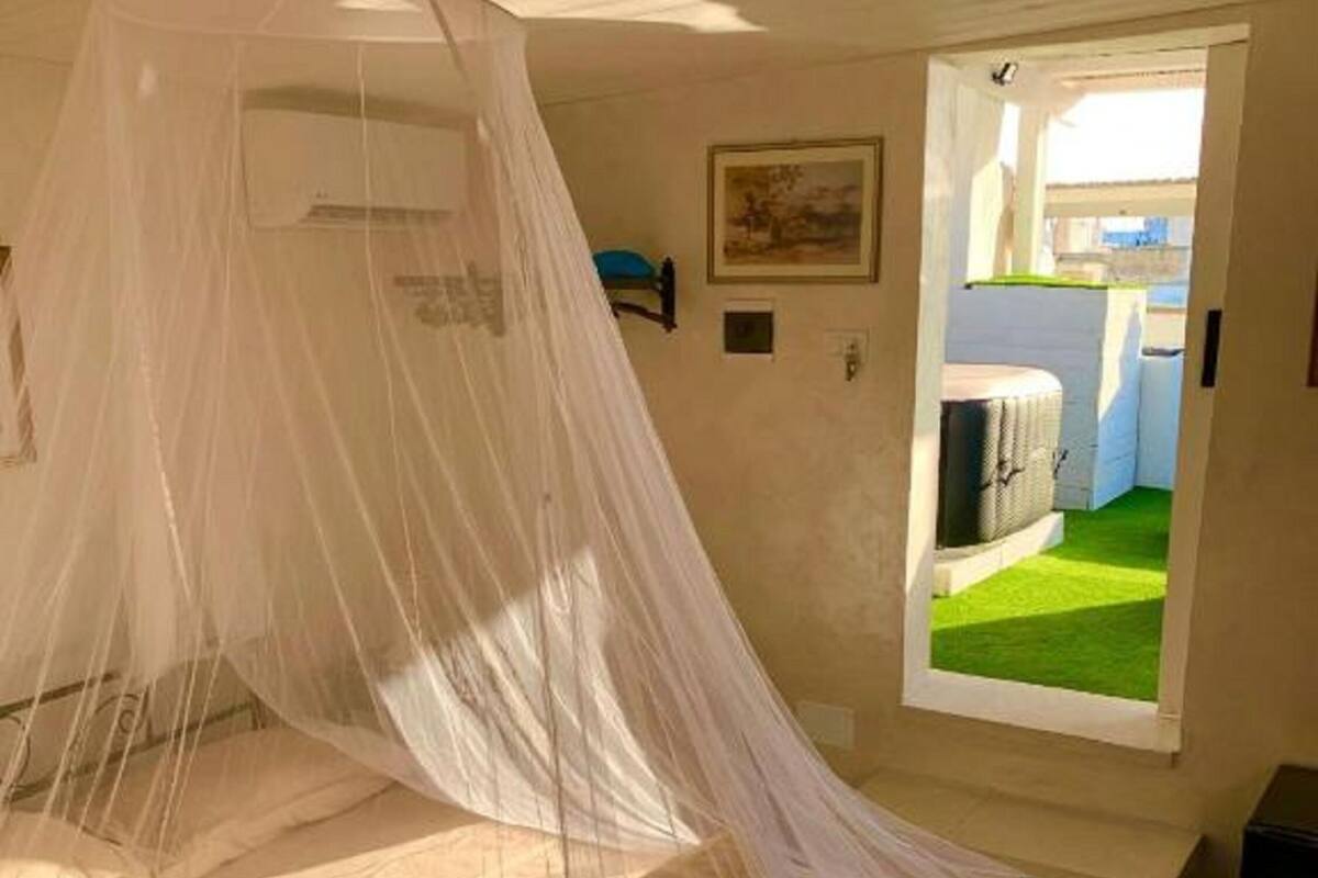 A bedroom with a bed covered by a white canopy, a window with a view of a green lawn, and a small bedside table.